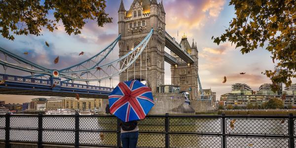 A tourist in front of London's Tower Bridge, with a Union Jack umbrella.