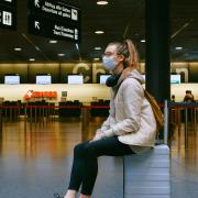 Woman sits in an airport while wearing a mask.