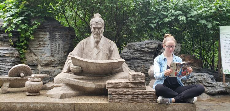 Student poses next a statue in China