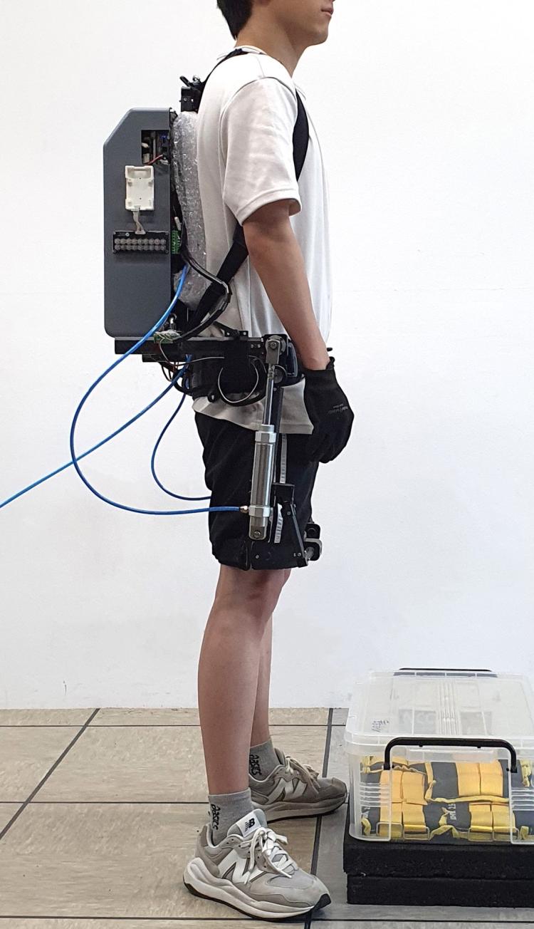 Man seen from the chin down wears a robotic device that looks like a backpack