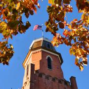 Old Main with an American flag on top of the tower framed by yellow autumn leaves and backed by a clear blue sky. (Photo by Casey A. Cass/University of Colorado)