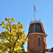 The tower of old main against a blue sky, framed by a branch of yellow leaves.