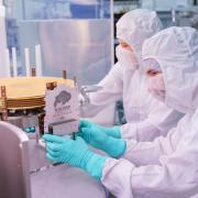 People in protective suits place a plaque on a space instrument in a clean room