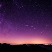 stars shine in a pink and purple sky above the mountains