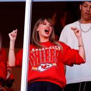 Taylor Swift cheering in a stadium box wearing a Kansas City Chiefs sweatshirt